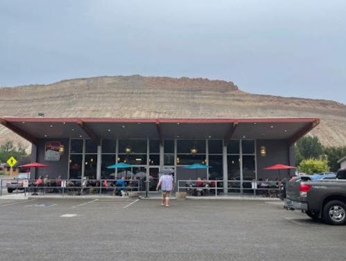 A restaurant with outdoor seating, set against a large rocky cliff under a cloudy sky.