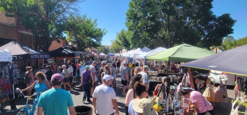 A bustling outdoor market with numerous tents, vendors, and a crowd of people enjoying the sunny day.