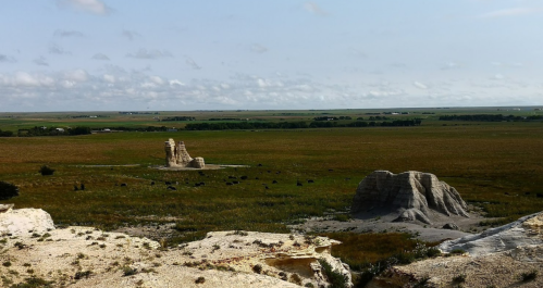 A wide view of a grassy landscape with rock formations under a cloudy sky in Nebraska.