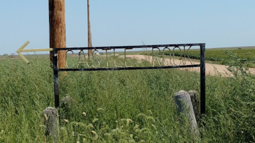 Sign for Castle Rock with an arrow pointing left, surrounded by tall grass and a dirt road in the background.