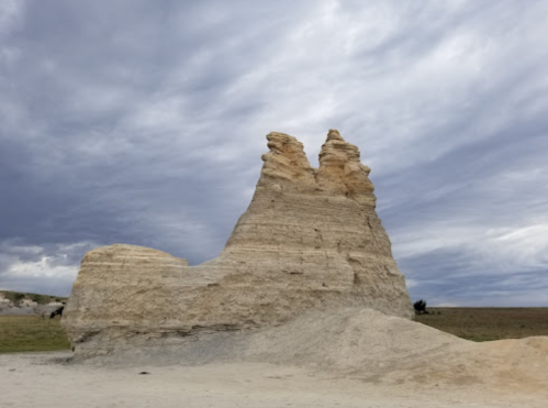A tall, weathered rock formation under a cloudy sky, resembling two peaks side by side in a barren landscape.