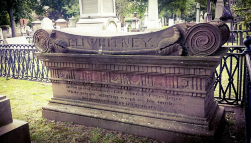 A weathered gravestone with the name "E. Whitney" and an inscription about a model of excellence in a cemetery.