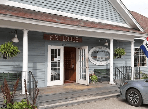 A quaint antique shop with a blue exterior, welcoming entrance, and a car parked outside.