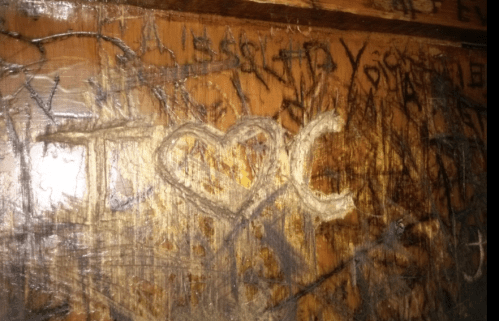 Carved message on wood reading "I ❤️ C," surrounded by other scratches and markings.