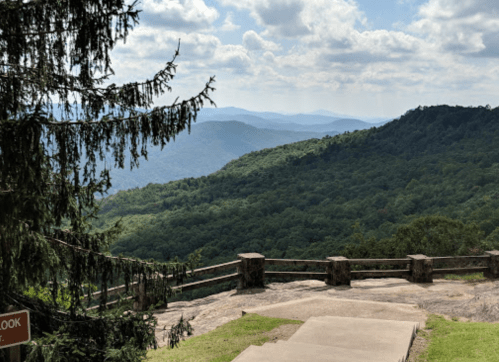 A scenic view of rolling green mountains under a partly cloudy sky, with a stone overlook in the foreground.