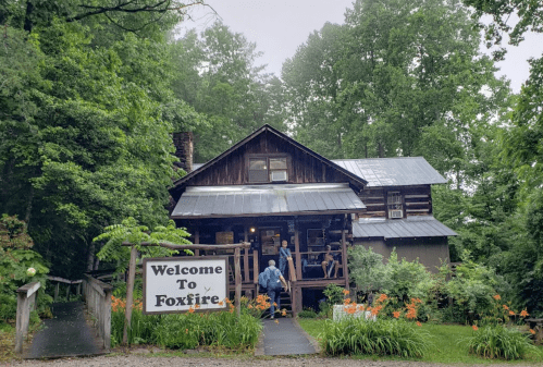 A rustic wooden building surrounded by greenery, with a sign reading "Welcome to Foxfire" in front.