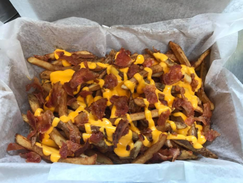 A box of crispy fries topped with melted cheese and crispy bacon bits.