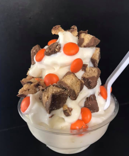 A cup of soft serve ice cream topped with chunks of chocolate candy and orange candy pieces.