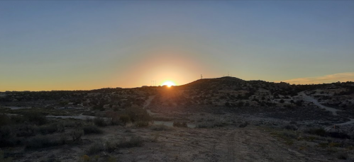 Sunrise over a rugged landscape, casting warm light on hills and a dirt path in the foreground.