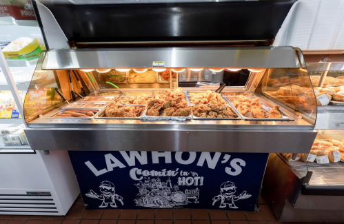 A display case filled with various fried foods, including chicken and hot dogs, labeled "Lawhon's Comin' in Hot!"