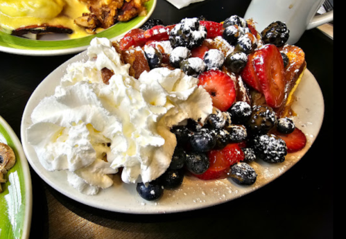 A plate of French toast topped with whipped cream, strawberries, blueberries, and powdered sugar.
