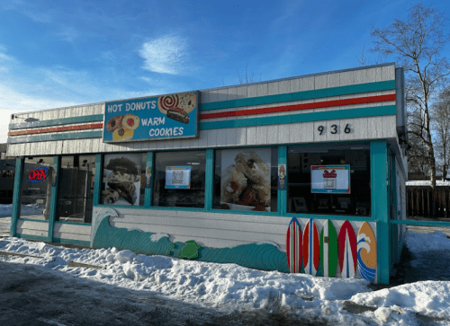 A colorful donut and cookie shop with a retro design, featuring surfboards and a snowy exterior.