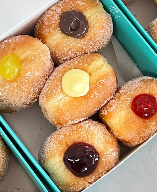 A box of sugar-coated donuts with colorful fillings: chocolate, yellow cream, and red jelly on top.