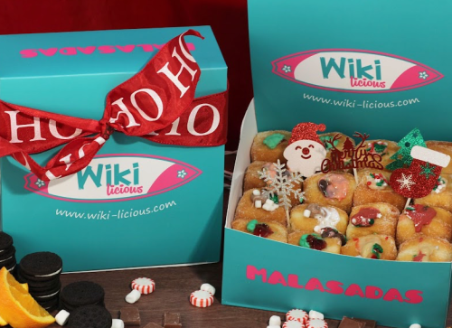 A festive box of colorful malassadas with holiday decorations, alongside a gift box wrapped in a red ribbon.