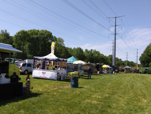 A food truck event with various tents and food vendors set up on a grassy field under a clear blue sky.