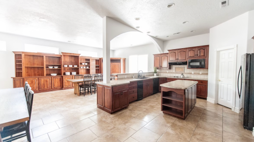 Spacious kitchen with wooden cabinets, an island, and a dining area featuring a large table and chairs. Bright and airy.