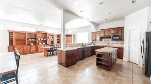 Spacious kitchen with wooden cabinets, an island, and a dining area featuring a large table and chairs. Bright and airy.