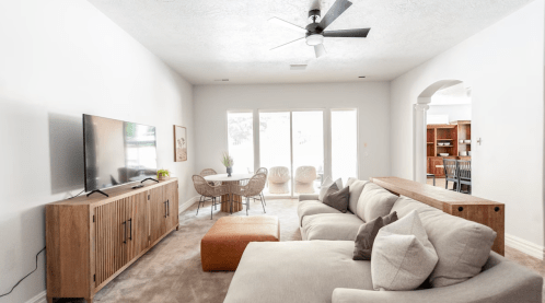 A modern living room with a beige sectional sofa, TV, and dining area featuring a round table and wicker chairs.