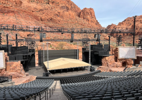 An outdoor amphitheater with a stage set against red rock formations and empty seating.