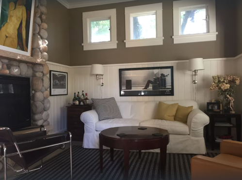 Cozy living room with a white sofa, stone fireplace, artwork, and large windows letting in natural light.