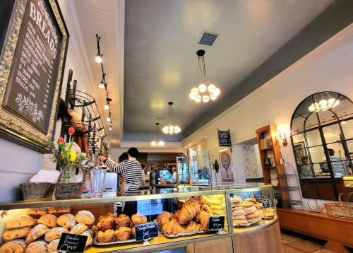 A cozy bakery interior with a display of pastries, a chalkboard menu, and a barista preparing orders.