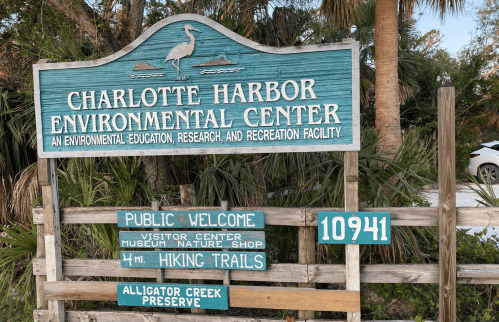 Sign for Charlotte Harbor Environmental Center, featuring visitor information and hiking trails, surrounded by greenery.