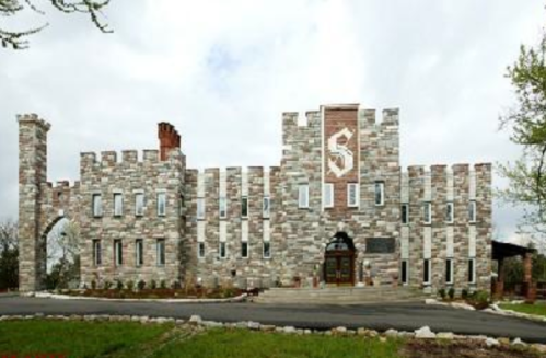 A large stone castle with a central entrance and decorative elements, set against a cloudy sky.