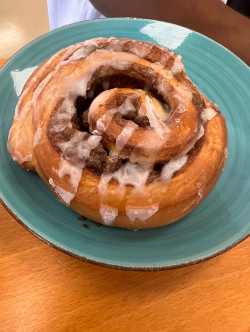 A large cinnamon roll with icing on a teal plate, resting on a wooden table.