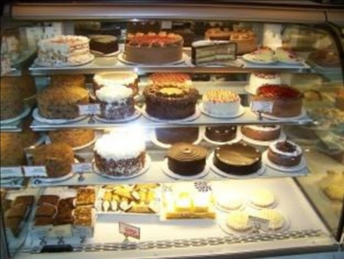 A display case filled with various cakes and desserts, including layered cakes, cheesecakes, and pastries.