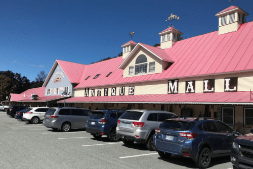 A large antique mall with a pink roof and multiple parked cars in front under a clear blue sky.
