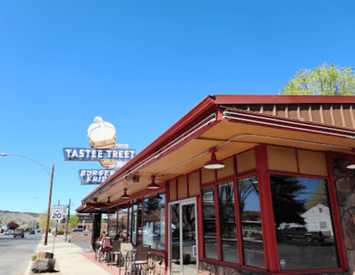 A diner named "Tastee Tree" with a retro sign, outdoor seating, and clear blue sky in the background.