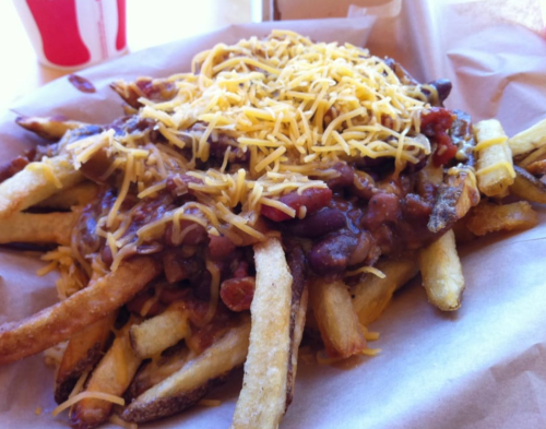 A plate of loaded fries topped with melted cheese and chili, served on brown paper.