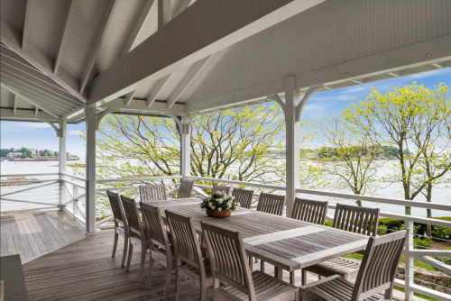 A spacious outdoor dining area with a large table, surrounded by trees and a view of the water.