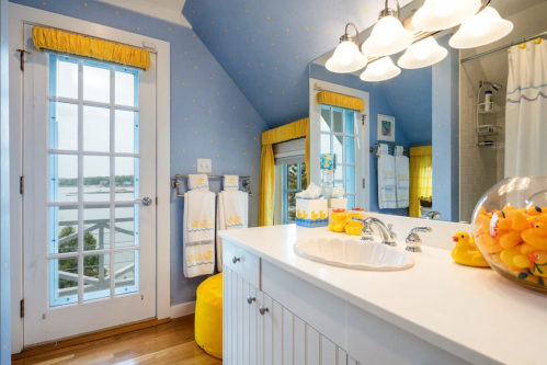 Bright bathroom with blue walls, yellow accents, a window, and decor featuring rubber ducks.