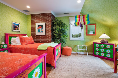 Brightly colored bedroom with green walls, floral bedding, and playful decor, featuring two beds and a cozy seating area.