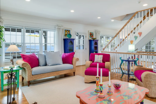Bright living room with colorful sofas, a coffee table, and large windows overlooking a scenic view.