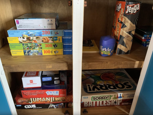 A wooden shelf filled with various board games and puzzles, including Jenga, Battleship, and Jumanji.
