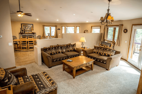 Cozy living room with brown sofas, a wooden coffee table, and large windows, leading to a dining area in the background.