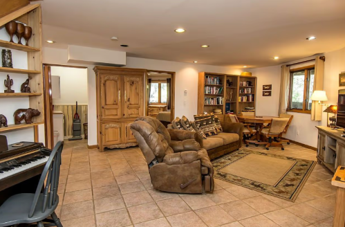 Cozy living space with a piano, comfortable seating, bookshelves, and a desk, featuring warm lighting and tiled flooring.