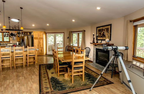Cozy dining area with wooden furniture, a telescope, and a view of the outdoors through large windows.