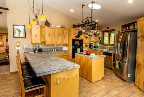 A spacious kitchen with wooden cabinets, a large island, and stainless steel appliances, featuring pendant lighting.