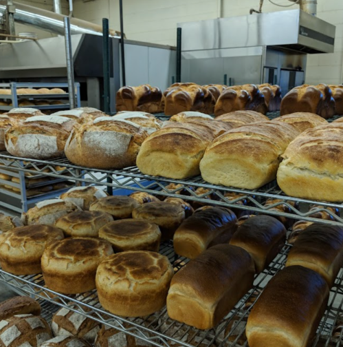 A variety of freshly baked loaves of bread arranged on wire racks in a bakery.