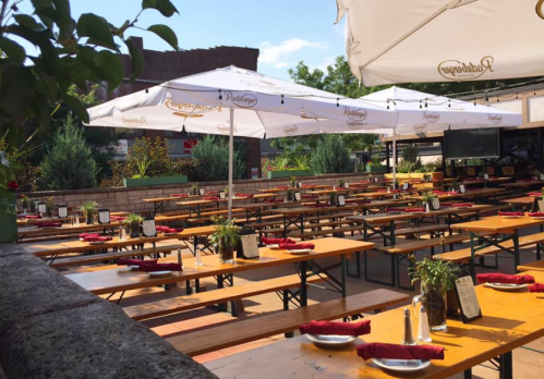 Outdoor dining area with wooden tables, umbrellas, and neatly arranged plates and utensils. Bright and inviting atmosphere.