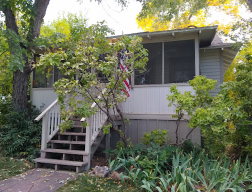 A charming house with a porch, surrounded by greenery and a small American flag on display.