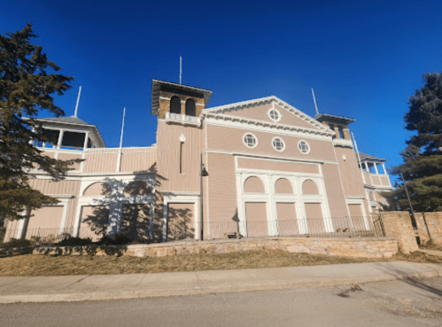 A large, light-colored building with a decorative facade and multiple roof structures against a clear blue sky.
