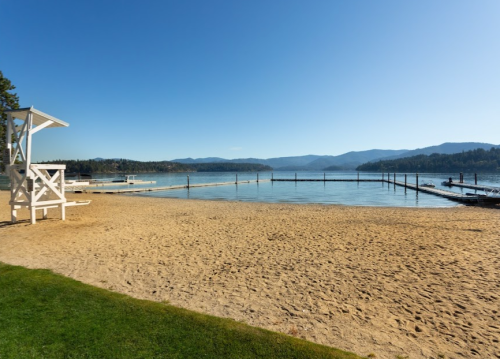 A sandy beach with a lifeguard tower, calm water, and distant mountains under a clear blue sky.