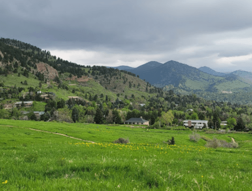 A scenic view of rolling green hills, houses nestled among trees, and mountains under a cloudy sky.