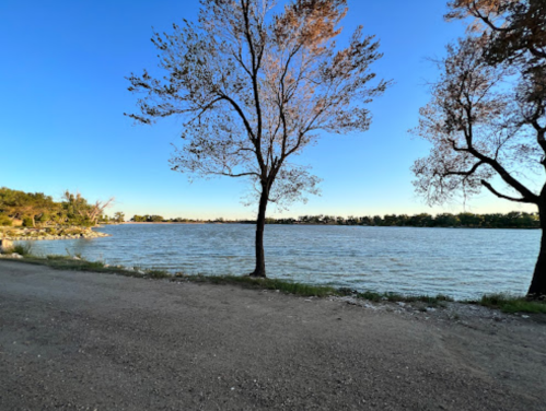 A serene lakeside view with trees on either side and a clear blue sky above.