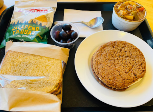 A tray with a sandwich cookie, bread, grapes, chips, and a cup of fruit salad.