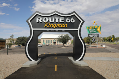 Sign for Route 66 in Kingman, Arizona, featuring a large archway and nearby museum signage. Clear blue sky above.